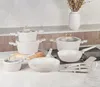 A collection of white cookware with gold accents is displayed on a kitchen counter. Produktbild-Vorschau