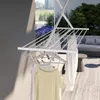 A clothes drying rack is set up on a balcony with clothes hanging on it. In the background, there is outdoor furniture and greenery. Podgląd zdjęcia produktu