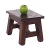 A small, dark brown wooden stool with a green apple on top, set against a white background. Produktbild-Vorschau
