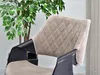 A close-up shot of a designer chair with a quilted beige seat and black frame, placed next to a potted plant. Podgląd zdjęcia produktu