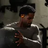 A man is holding a large medicine ball in a gym setting, wearing orange earbuds. Náhled obrázku produktu