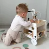 A baby is playing with a wooden activity walker on a play mat. Produktbild-Vorschau