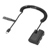 A black coiled USB-C cable with a dummy battery coupler attached to the end, set against a white background. Produktbild-Vorschau