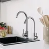 A kitchen sink with two faucets and some kitchen utensils in the background. Anteprima dell’immagine prodotto