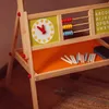A close-up shot of a wooden easel for children, featuring a clock, an abacus, and a tray with chalk and an eraser. Produktbild-Vorschau