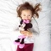A young girl lying on a bed holding a Minnie Mouse plush toy. Produktbild-Vorschau