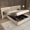 A modern bedroom with a beige upholstered storage bed, open to reveal storage compartments. Two bedside tables with charging devices are attached to the headboard. Náhled obrázku produktu
