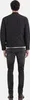 A person wearing a black quilted jacket and dark jeans, viewed from the back. Produktbild-Vorschau