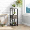 A tall, narrow plant stand with three shelves and a drawer, placed next to a white brick wall and a window. Several potted plants are displayed on the shelves. Produktbild-Vorschau