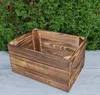 A wooden storage box sits on a light gray surface in front of a green hedge. Náhled obrázku produktu