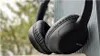 A pair of black Sony headphones rests against a wooden surface, with a blurred background of trees and foliage. Anteprima dell’immagine prodotto