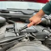 A person's hand is using a torque wrench to tighten a bolt on a car engine. Voir les images du produit