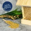 A bird feeder filled with birdseed, a scoop of birdseed, and some artificial grass and a branch are arranged on a gray surface. Produktbild-Vorschau