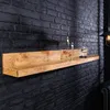 A wooden shelf mounted on a black brick wall, decorated with two candle holders and a glass dome with a bottle inside. Produktbild-Vorschau