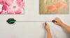 A person is using a digital laser level and tape measure to hang a picture on a wall. Produktbild-Vorschau