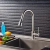 A kitchen faucet is shown in front of a textured black backsplash, with a sink and some fruit in the foreground. Náhľad obrázku produktu