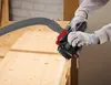 A person wearing work gloves is using a cordless planer on a wooden surface, with a vacuum hose attached. Produktbild-Vorschau