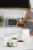 A woman is standing in a kitchen, near a microwave, with several white storage containers on the counter. Produktbild-Vorschau