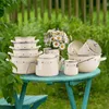 A collection of cream-colored enamel cookware with red heart and arrow accents is arranged on a teal-colored table outdoors, with a bouquet of daisies in a vase. Produktbild-Vorschau