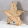A wooden star decoration is placed on a white surface against a gray concrete wall. Produktbild-Vorschau