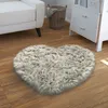 A heart-shaped fluffy rug is placed on a wooden floor in a room with a white sofa and a white dresser. Produktbild-Vorschau