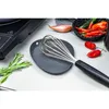 A whisk resting on a gray spoon rest, with ingredients like shallots and chili peppers in the background. Produktbild-Vorschau