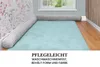 A baby bed bumper snake is placed around a light blue rug in a nursery room, next to a window and a floral wallpaper. Produktbild-Vorschau