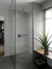 A modern bathroom with a glass-enclosed shower and a plant on a wooden bench. Produktbild-Vorschau