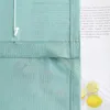 A close-up view of a green fabric blind with text printed on a piece of paper behind it. Two lemons are visible in the lower right corner. Produktbild-Vorschau