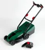 A green toy lawnmower with black handles and wheels, shown on a white background. A detached red and black accessory is in the foreground. Produktbild-Vorschau