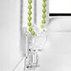 A close-up of a green beaded pull cord for a window blind, attached to a clear plastic bracket mounted on a white wall. Produktbild-Vorschau