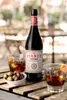 A bottle of Lustau Vermut Red is displayed on a wooden table with two glasses of the drink, ice, orange slices, and a bowl of olives. Produktbild-Vorschau