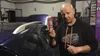 A man in a garage holds up a bottle of automotive additive next to a car. Produktbild-Vorschau