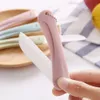 A hand holding a pink ceramic fruit peeler with other peelers in pastel colors in the background, along with some fruit on a striped cloth. Voir les images du produit