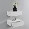 Two white floating shelves mounted on a gray wall. The top shelf holds a black vase with white flowers. The bottom shelf has a drawer partially open and a small decorative picture frame on top. Voir les images du produit