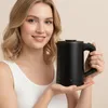 A woman is holding a black electric kettle. Produktbild-Vorschau
