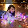 A young girl lies on a wooden floor surrounded by colorful LED string lights and decorative gnome figures. Produktbild-Vorschau