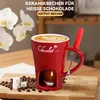A red ceramic mug designed for hot chocolate, with a candle underneath to keep it warm, surrounded by coffee beans and sugar cubes. Produktbild-Vorschau