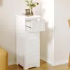 A white wooden cabinet with four drawers, one of which is open, sits in a room with a light-colored wall and wooden floor. A bouquet of flowers and books are on top of the cabinet. Produktbild-Vorschau