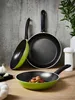 Three frying pans are arranged on a wooden surface in front of a concrete wall. One pan is in the foreground with food inside, and two others are in the background. Produktbild-Vorschau
