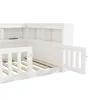 A close-up, angled view of a white wooden children's bed with a slatted base and a built-in bookshelf unit. Náhľad obrázku produktu