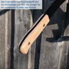 Close-up of a wooden handle with a black metal part, set against a wooden fence background. Produktbild-Vorschau