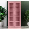 A pink metal cabinet with glass doors and shelves, flanked by two potted plants against a white and dark green background. Produktbild-Vorschau