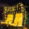 A garden swing decorated with string lights and vines at night. Náhled obrázku produktu