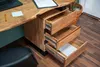 A close-up view of a wooden desk with three open drawers, showing the interior and drawer slides. A laptop and a document are visible on the desk surface. Produktbild-Vorschau