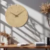 A minimalist wall clock with a stone-like texture is displayed on a wall above a wooden desk with a book and decorative plants. Produktbild-Vorschau