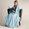 A woman is sitting in a chair wrapped in a light blue blanket and reading a book. Podgląd zdjęcia produktu