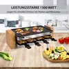 A raclette grill with food on top and in the trays, set on a wooden table with some vegetables and a cheese platter. Produktbild-Vorschau