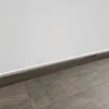 A close-up view of a white baseboard and a wooden floor. Produktbild-Vorschau