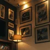 A corner of a room with framed pictures on the wall and a floor lamp. Anteprima dell’immagine prodotto